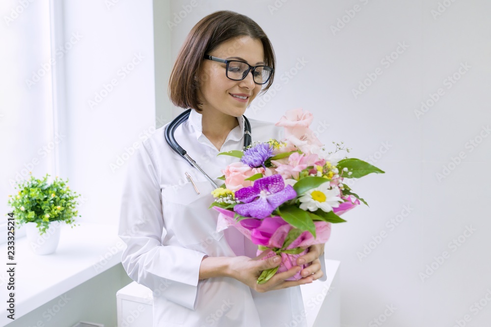 Woman doctor with bouquet of flowers, smiling near the window in the hospital. National Doctor's day. Woman doctor with bouquet of flowers, smiling near the window in the hospital. National Doctor's day.