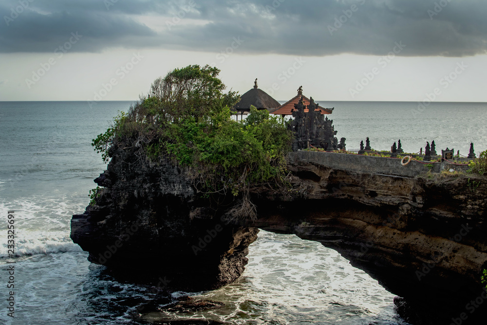 Chimeric temple on the water. Water temple in Bali. Indonesia nature landscape. Famous Bali landmark. Splashing waves and stone. Cloudy day in Indonesia. Water and rocks before storm