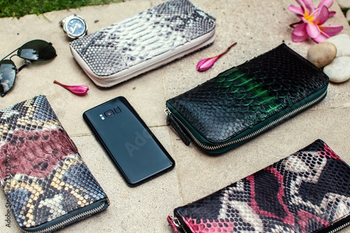 Exotic and luxury set of hand made leather wallet .Multi colored.Leather craft. On a stone tile with background with Plumeria .Python piton snake fashionable handbag, purse,clutch.Python accessories
