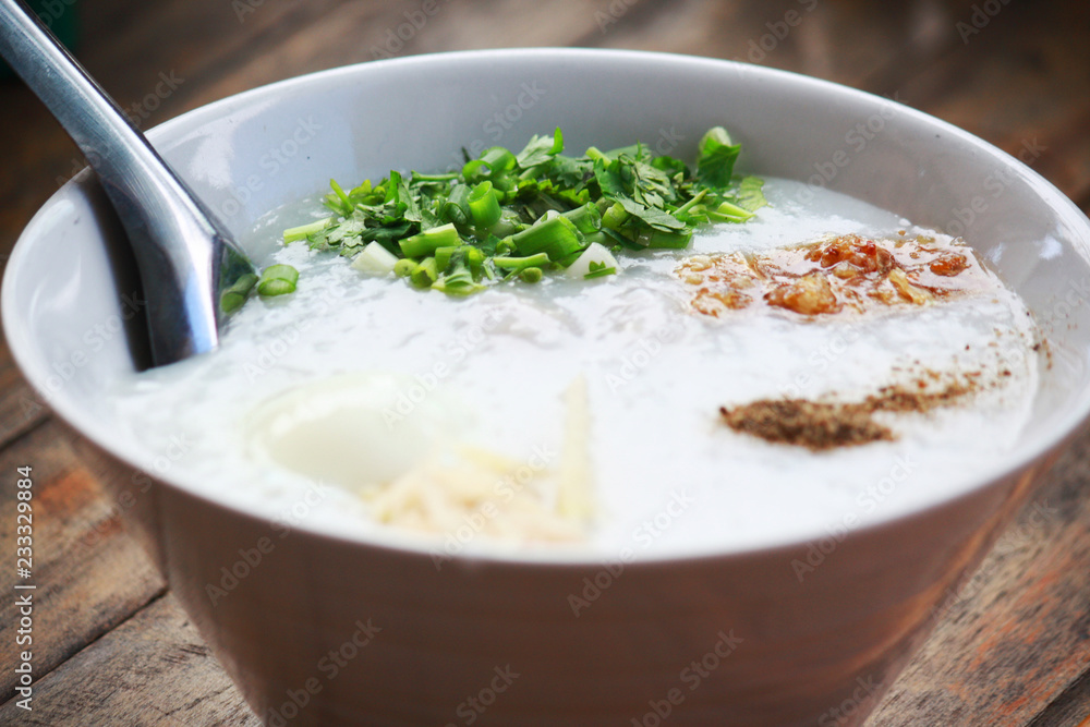 Thai Rice Soup With pork,egg, sginger and vegetable in white bowl.Rice porridge with ingredient condiments.