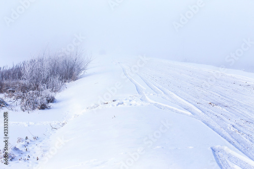 Christmas winter landscape of the frozen lake covered with snow on a cold winter day and the road in the mist 