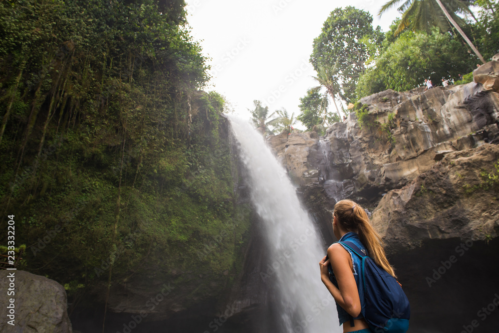 Young Blonde Woman with a Backpack Admiring a Majestic Waterfall in the ...