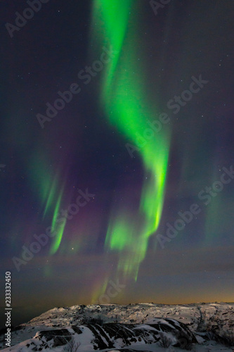 Beautiful northern lights, aurora in the night sky over the snow-covered hills. © Moroshka