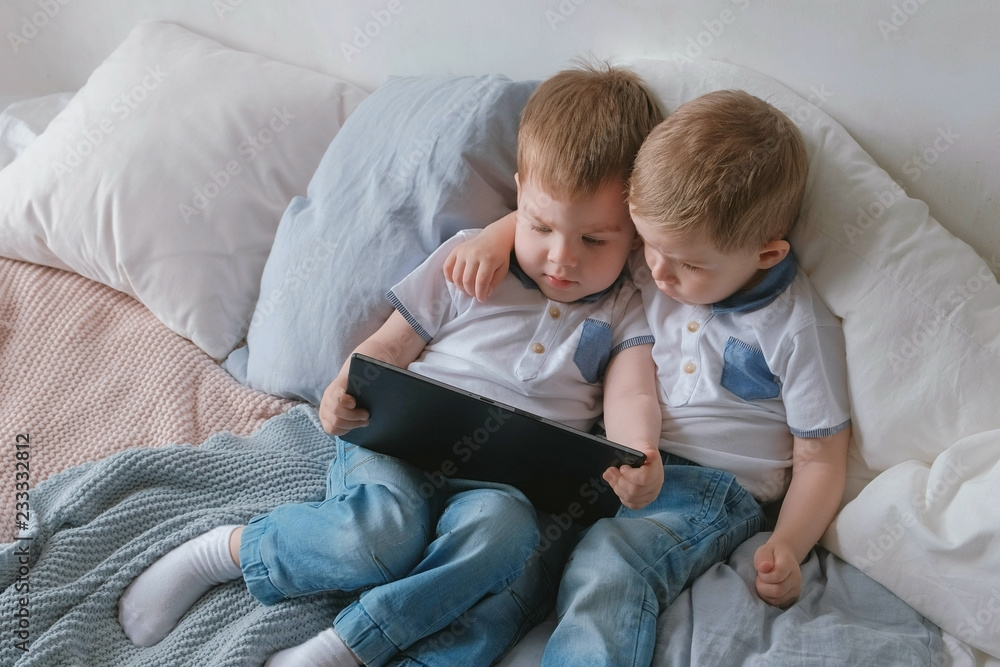 Kids with tablet. Two boys twins toddlers looking cartoon at tablet lying on the bed. Kids with tablet. Two boys twins toddlers looking cartoon at tablet lying on the bed.