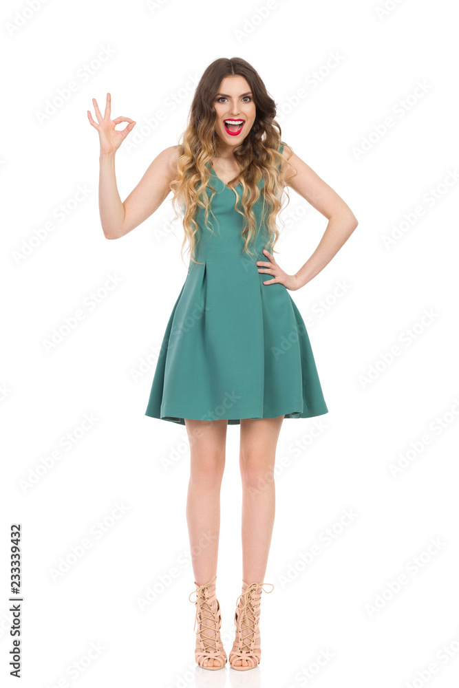 Beautiful Young Woman In Green Mini Dress And High Heels Is Showing Ok Hand Sign And Talking