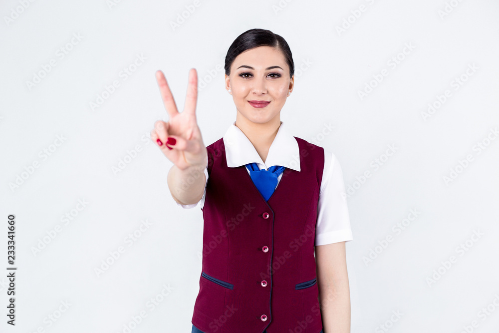 Beautiful girl stewardess in red uniform stands on white background showing two fingers Beautiful girl stewardess in red uniform stands on white background showing two fingers