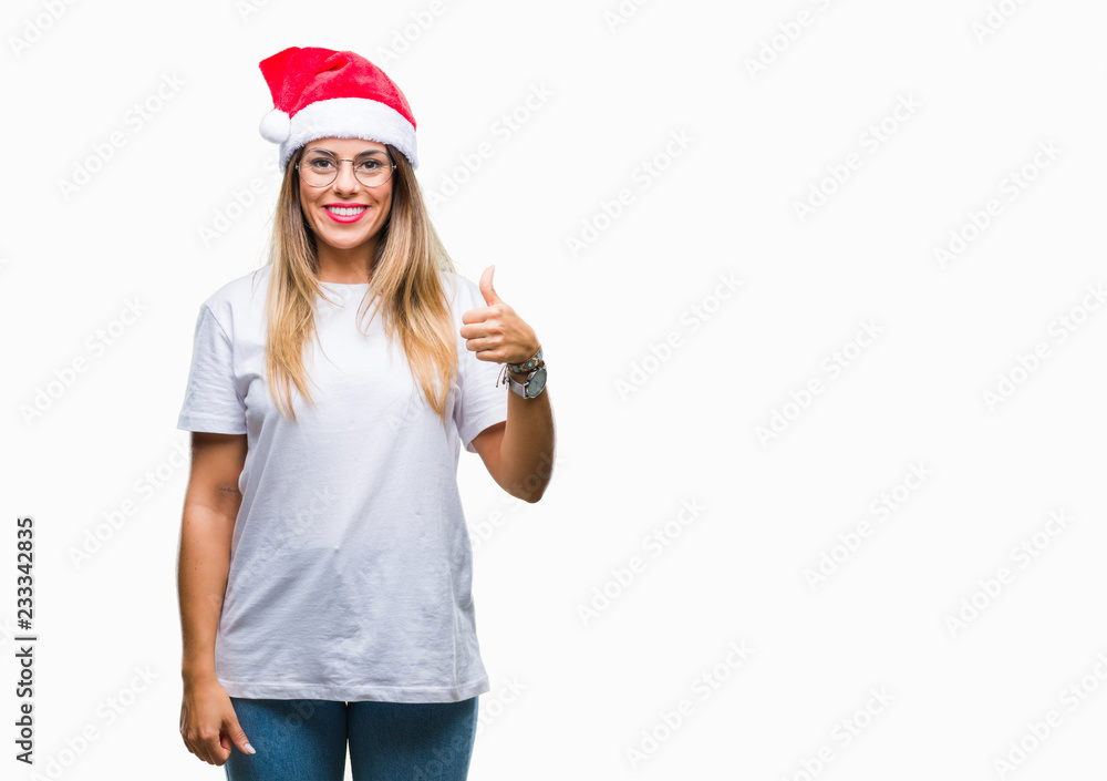 Young beautiful woman wearing christmas hat over isolated background doing happy thumbs up gesture with hand. Approving expression looking at the camera with showing success. Young beautiful woman wearing christmas hat over isolated background doing happy thumbs up gesture with hand. Approving expression looking at the camera with showing success.