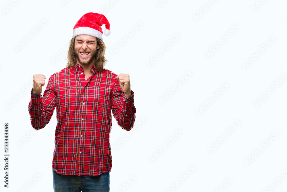 Young handsome man with long hair wearing santa claus hat over isolated background very happy and excited doing winner gesture with arms raised, smiling and screaming for success. Celebration concept. Young handsome man with long hair wearing santa claus hat over isolated background very happy and excited doing winner gesture with arms raised, smiling and screaming for success. Celebration concept.