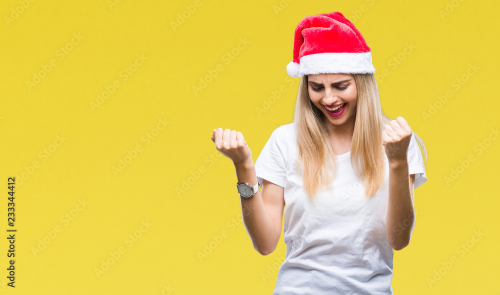 Young beautiful blonde woman christmas hat over isolated background very happy and excited doing winner gesture with arms raised, smiling and screaming for success. Celebration concept. Young beautiful blonde woman christmas hat over isolated background very happy and excited doing winner gesture with arms raised, smiling and screaming for success. Celebration concept.