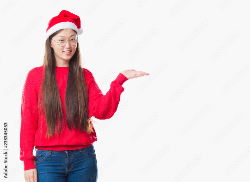Young Chinese woman over isolated background wearing christmas hat smiling cheerful presenting and pointing with palm of hand looking at the camera. Young Chinese woman over isolated background wearing christmas hat smiling cheerful presenting and pointing with palm of hand looking at the camera.