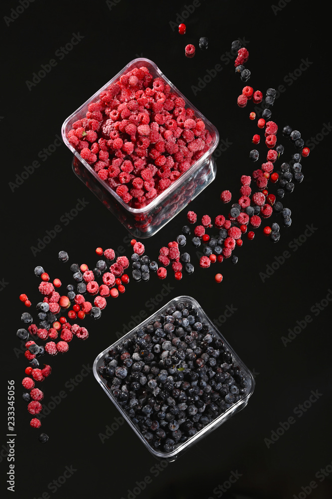Frozen raspberry and blueberry berries in glass bowls on a dark background.