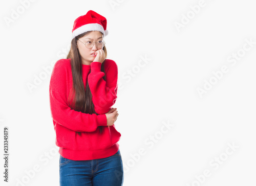 Young Chinese woman over isolated background wearing christmas hat looking stressed and nervous with hands on mouth biting nails. Anxiety problem.