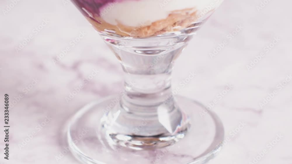 Figs pudding parfait with yogurt, blueberry jam, figs, hazelnut, and cookies in glass on white marble background. Flatlay top view.