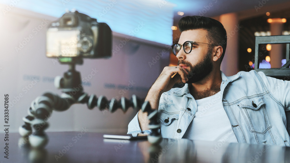 Bearded male video blogger creates video content for his channel. Man vlogger relieves himself on camera with tripod. Bearded male video blogger creates video content for his channel. Man vlogger relieves himself on camera with tripod.