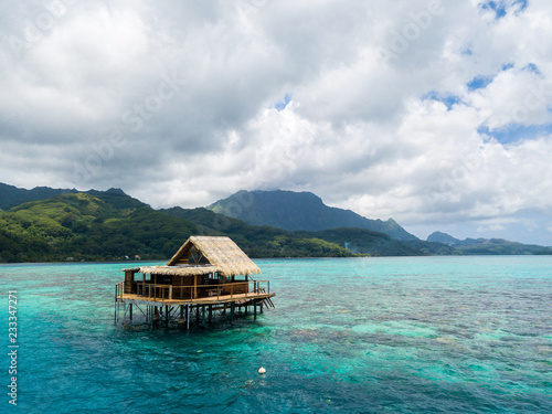 Lonely overwater bungalow of black pearl farmers. Blue azure turquoise lagoon with corals. Emerald Raiatea island, French Polynesia, Oceania.