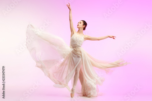 Young graceful female ballet dancer or classic ballerina dancing at pink studio. Caucasian model on pointe shoes
