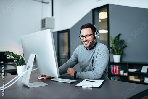 Tableau sur toile Smiling casual business man with headset working on the computer.