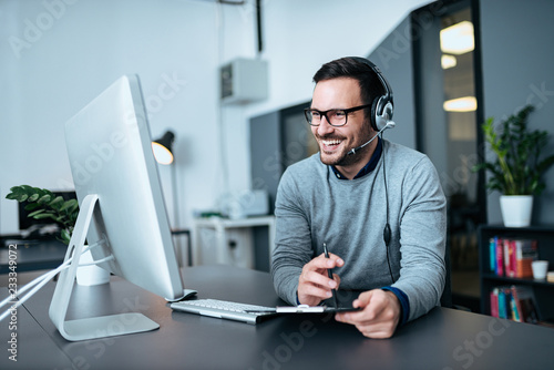 Portrait of a casual smiling businessman using headset when talking to customer. photo