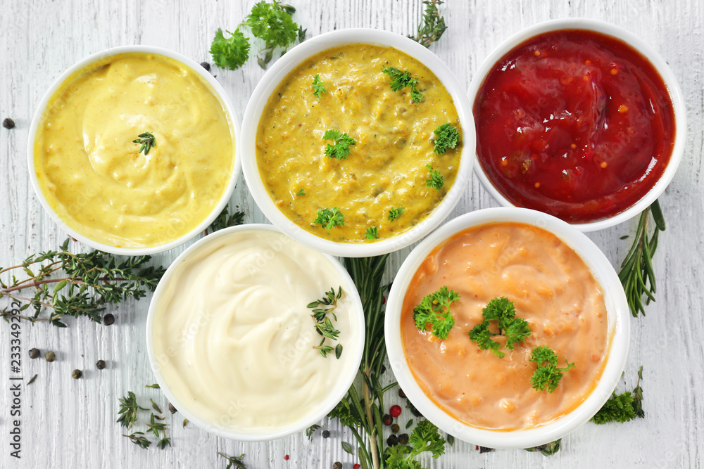 Different tasty sauces in bowls with spices on white wooden table Different tasty sauces in bowls with spices on white wooden table