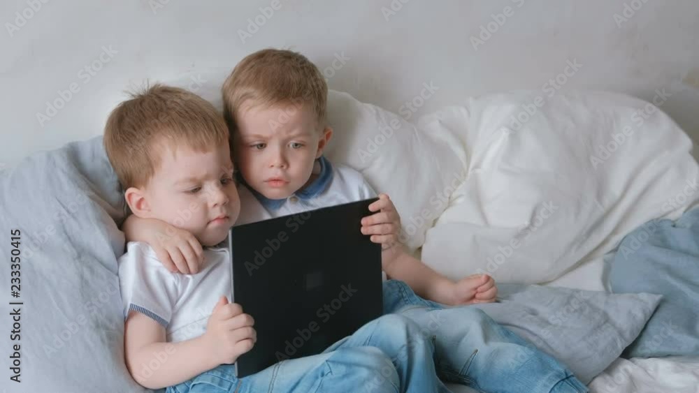 Kids with tablet. Two boys twins toddlers looking cartoon at tablet lying on the bed. Kids with tablet. Two boys twins toddlers looking cartoon at tablet lying on the bed.