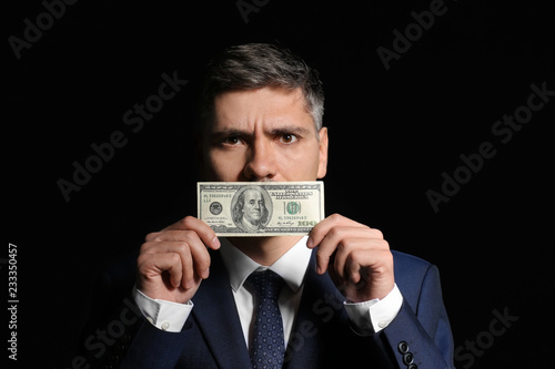 Businessman covering mouth with bribe on dark background. Corruption concept