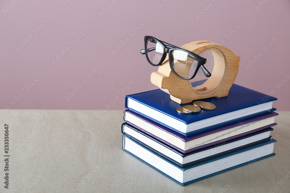Piggy bank, glasses and stack of books on table. Concept of savings for education Piggy bank, glasses and stack of books on table. Concept of savings for education