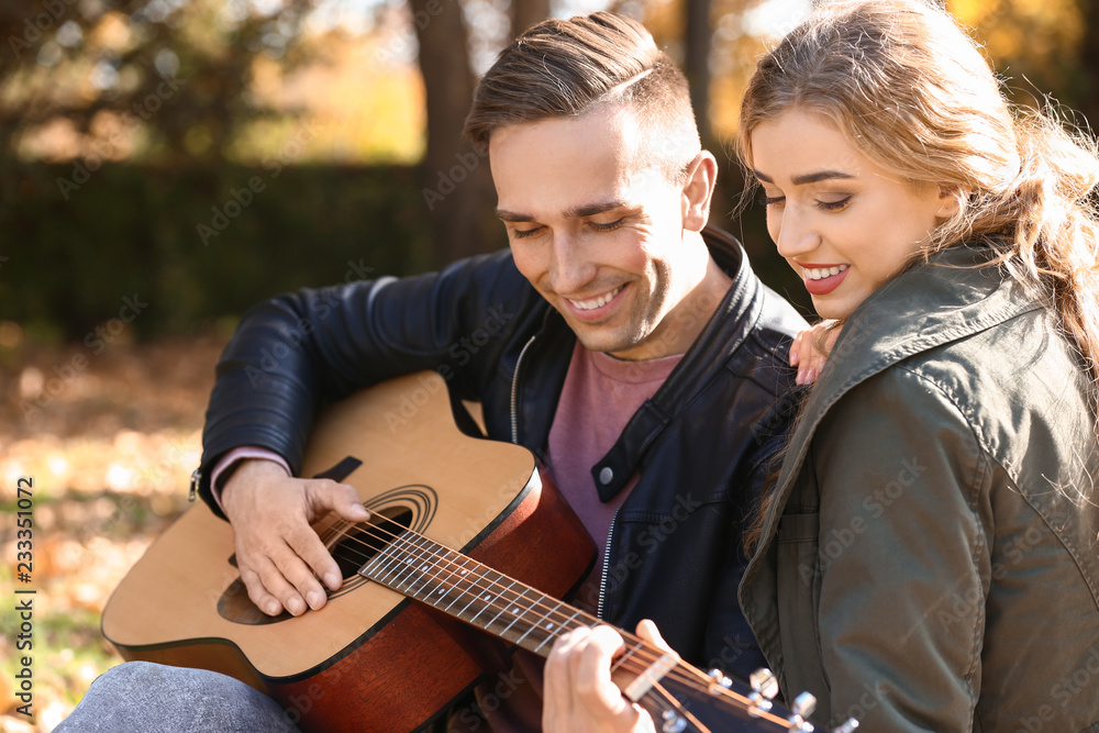 Handsome young man with guitar and his beloved resting in autumn park