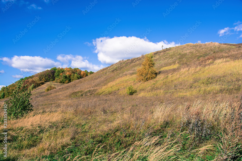 Bright autumn landscape with a cross on a mountain on a sunny day.