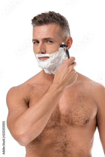 muscular shirtless man with foam on face shaving with razor isolated on white