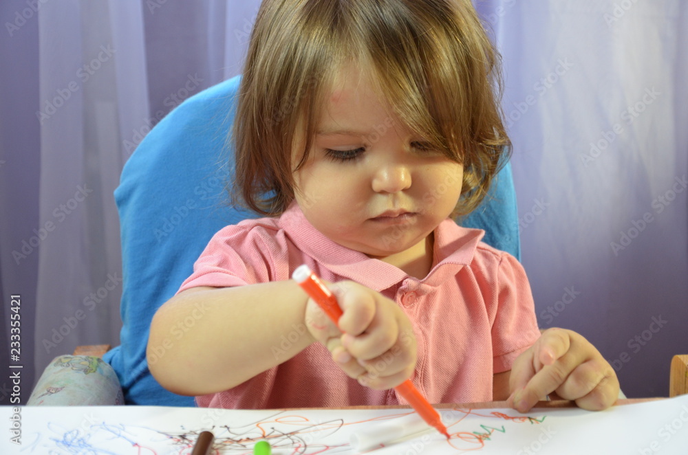 Cheerful little girl with sketch pen drawing on white paper in kindergarten or at home Cheerful little girl with sketch pen drawing on white paper in kindergarten or at home