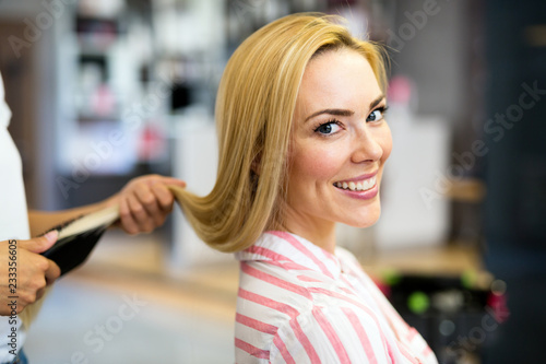 Happy young woman and hairdresser with fan making hot styling