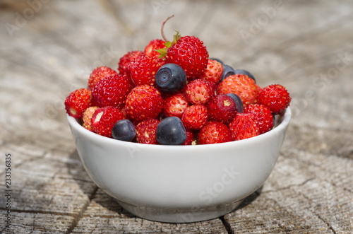 Fresh strawberries and blueberries in a porcelain bowl on a wooden stump