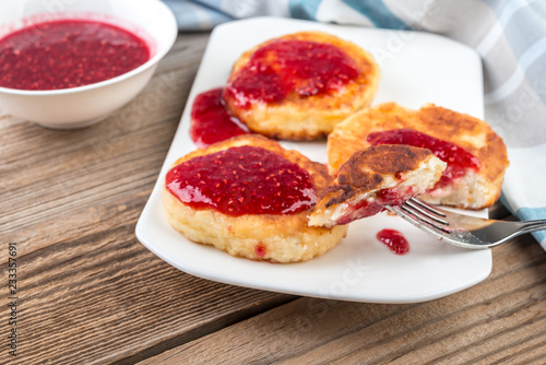 Cottage cheese pancakes, cheesecakes with raspeberry jam on wooden background, healthy traditional breakfast