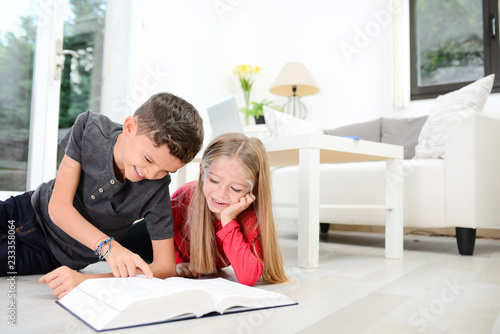 two young happy kids brother and sister together having fun at home reading encyclopedia book photo