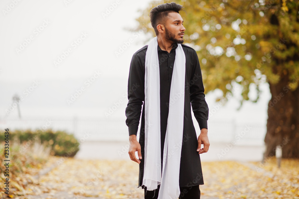 Indian stylish man in black traditional clothes with white scarf posed outdoor against autumn leaves tree. Indian stylish man in black traditional clothes with white scarf posed outdoor against autumn leaves tree.