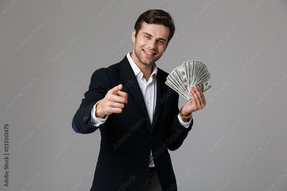 Image of successful businessman 30s in suit smiling and holding fan of money in dollar banknotes, isolated over gray background Image of successful businessman 30s in suit smiling and holding fan of money in dollar banknotes, isolated over gray background