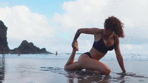 fitness girl or young woman in shape silhouette, surfer doing some stretching exersices on sandy beach, gymnastics. clolrful sky, calm sea or ocean, horizon, sandy beach or coast as background photo