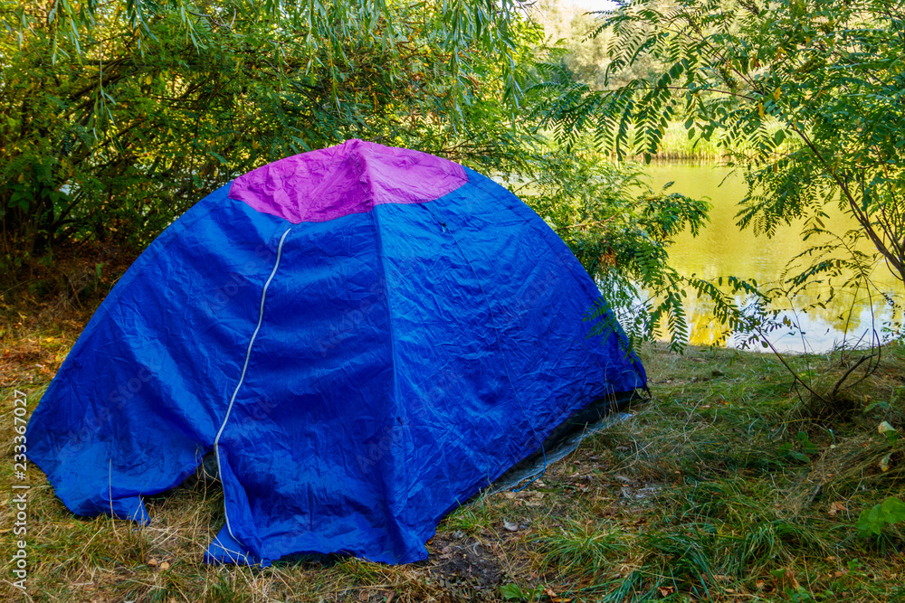 Blue camping tent in forest near a river