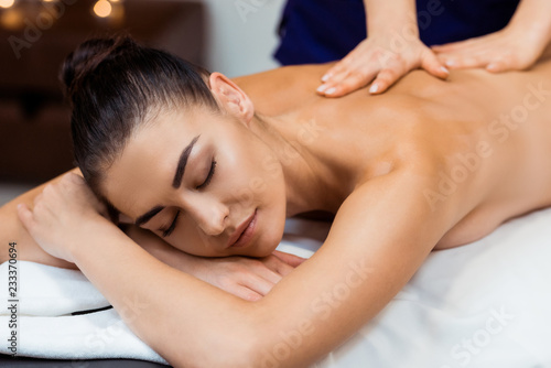 beautiful young woman with closed eyes having massage treatment in spa