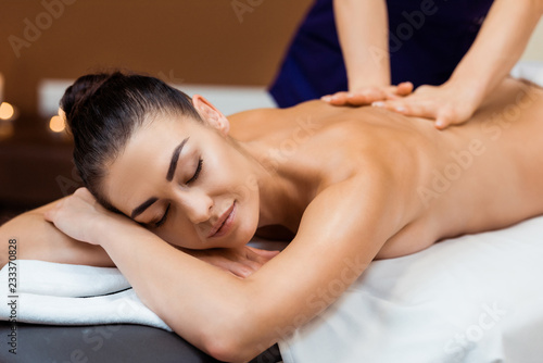 attractive smiling young woman with closed eyes enjoying massage in spa