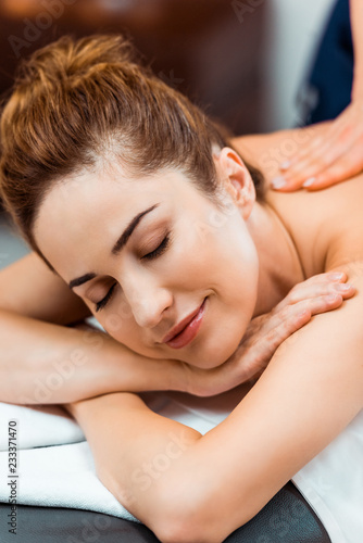 happy young woman with closed eyes enjoying massage in spa salon