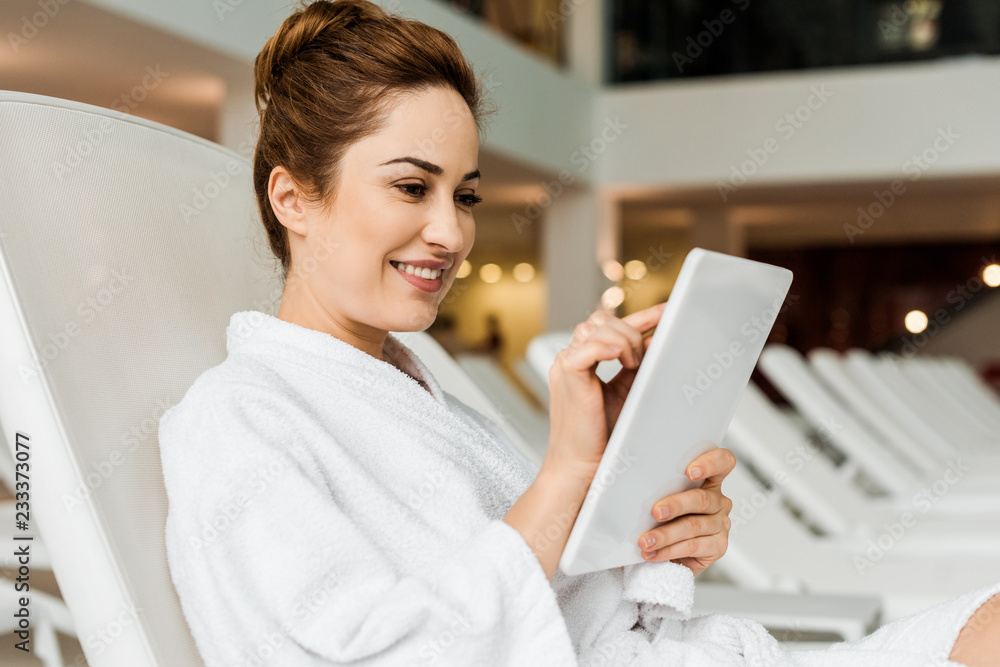 smiling young woman in bathrobe using digital tablet while relaxing in spa smiling young woman in bathrobe using digital tablet while relaxing in spa