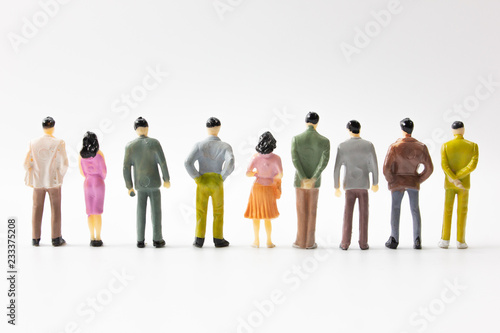 A group of miniature business people stand on white background back view closeup.