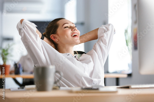 Happy young woman dressed in shirt sitting at her workplace photo