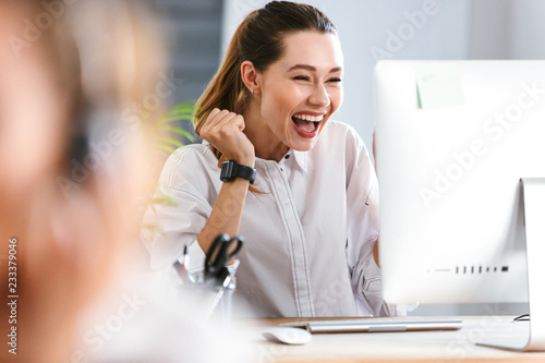 Happy young woman dressed in shirt sitting at her workplace