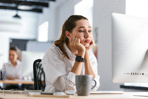 Bored young woman dressed in shirt sitting at her workplace photo