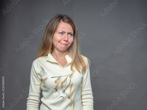 Blonde woman pulling funny face making an exaggerated grimace. Adult girl bulging eyes, pouts lips. Woman with awkward expressions of face has fun, plays fool. Portrait isolated on gray background