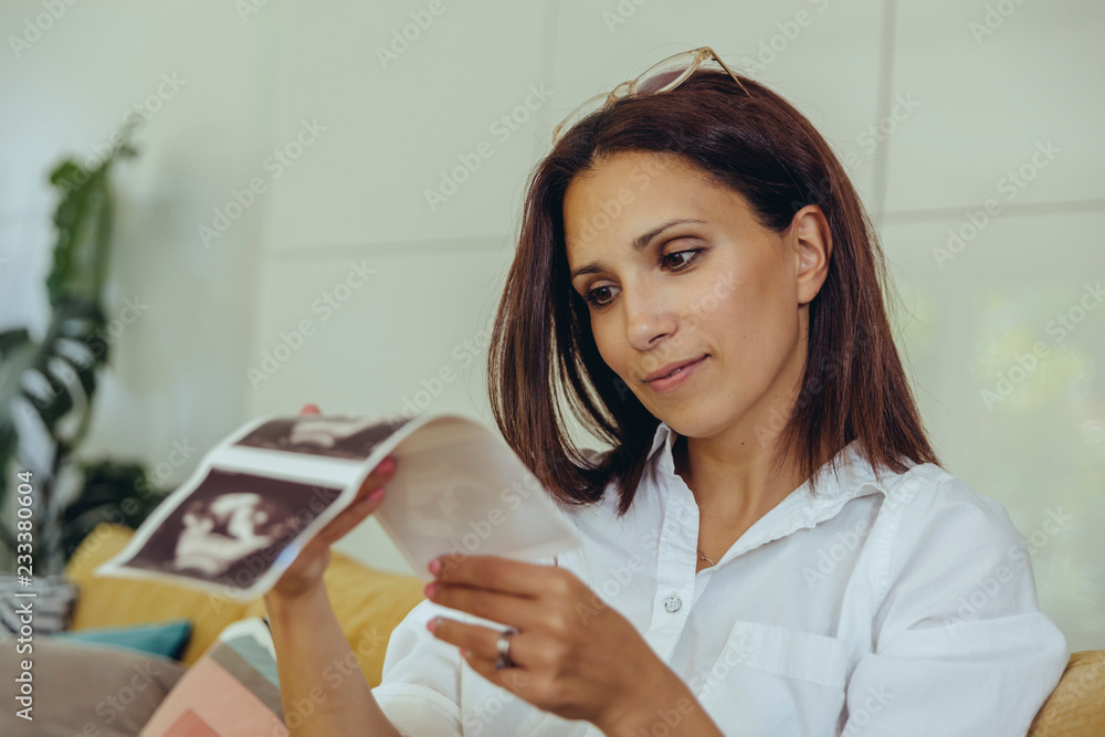 Woman looking at ultrasound pictures of unborn child on couch Woman looking at ultrasound pictures of unborn child on couch