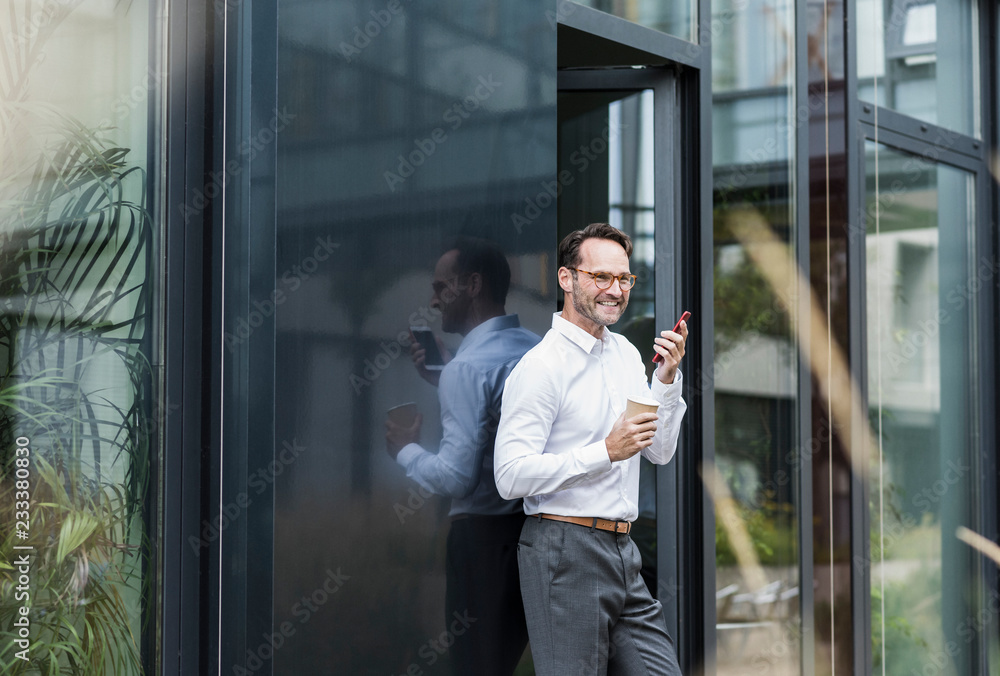 Businessman with coffee to go using cell phone in front of office building Businessman with coffee to go using cell phone in front of office building