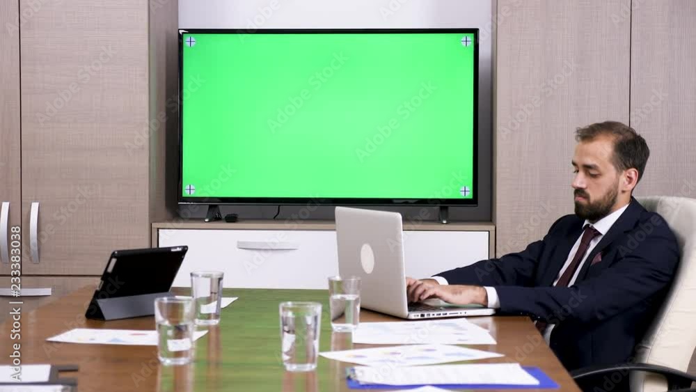 Businessman in meeting room working on computer next to a green screen TV. Dolly slider 4K footage Businessman in meeting room working on computer next to a green screen TV. Dolly slider 4K footage